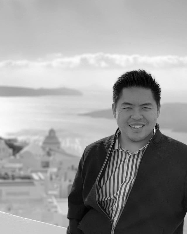 Andrew Wongso smiling in a blazer, sea and whitewashed buildings behind him