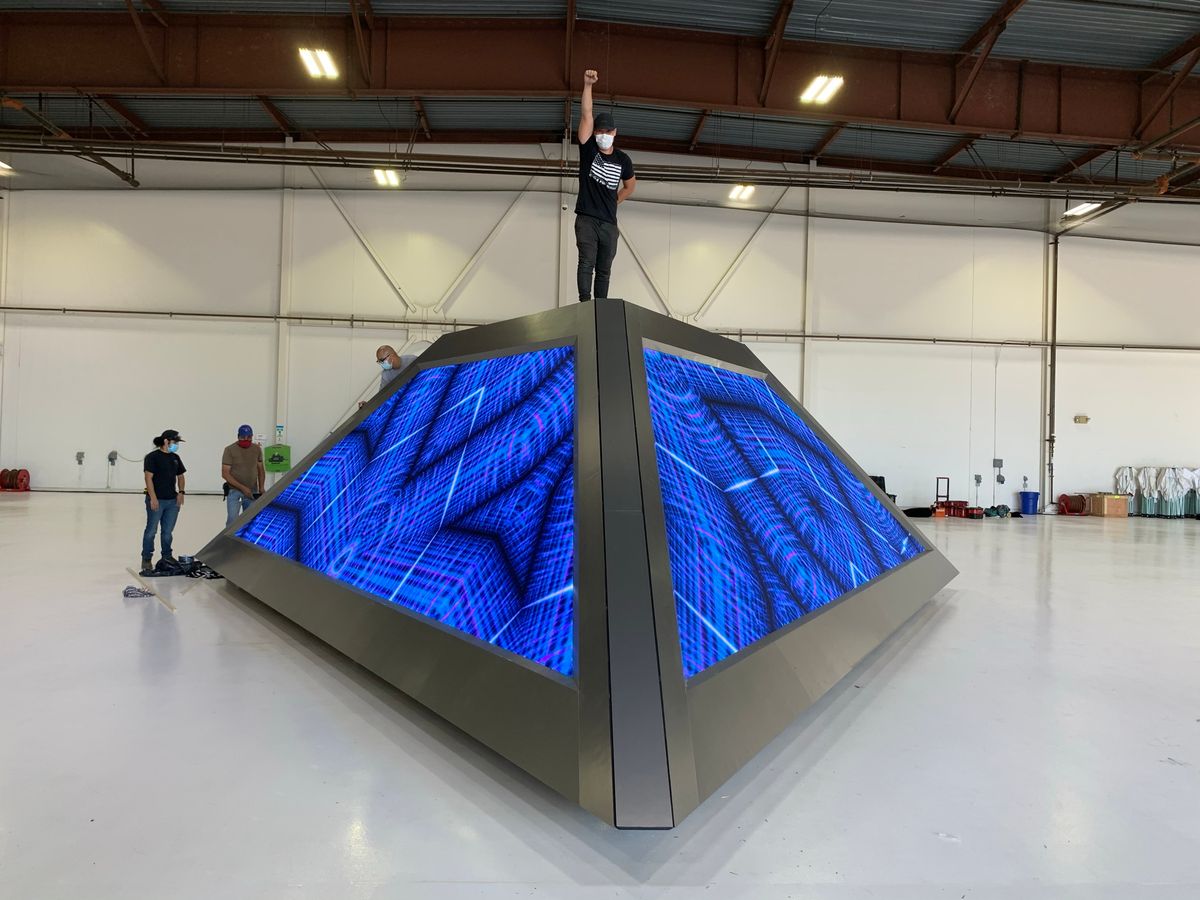 The finished LED pyramid in the hangar with blue content up, a crew member standing on its peak