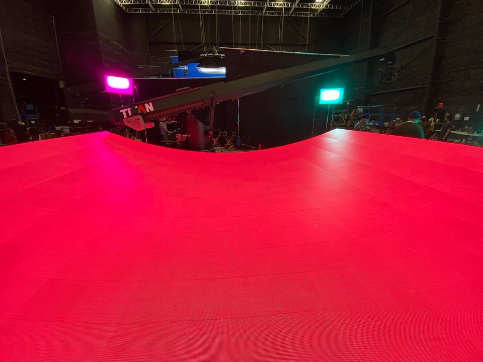The curved LED floor lit red, with the crane and the studio lights behind it