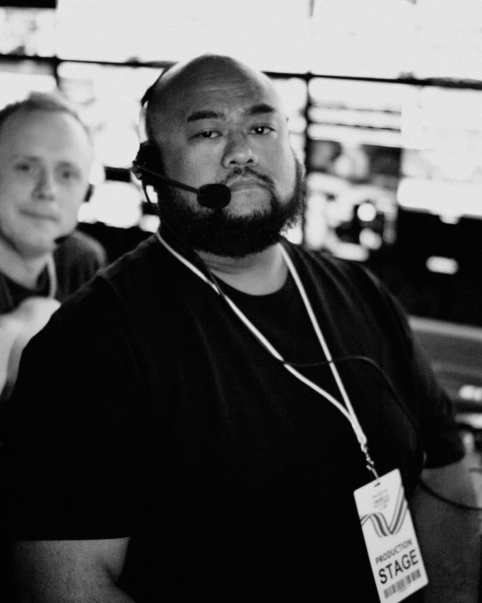 Eddie Suparman on a headset in the control room, black and white, wearing a production stage pass