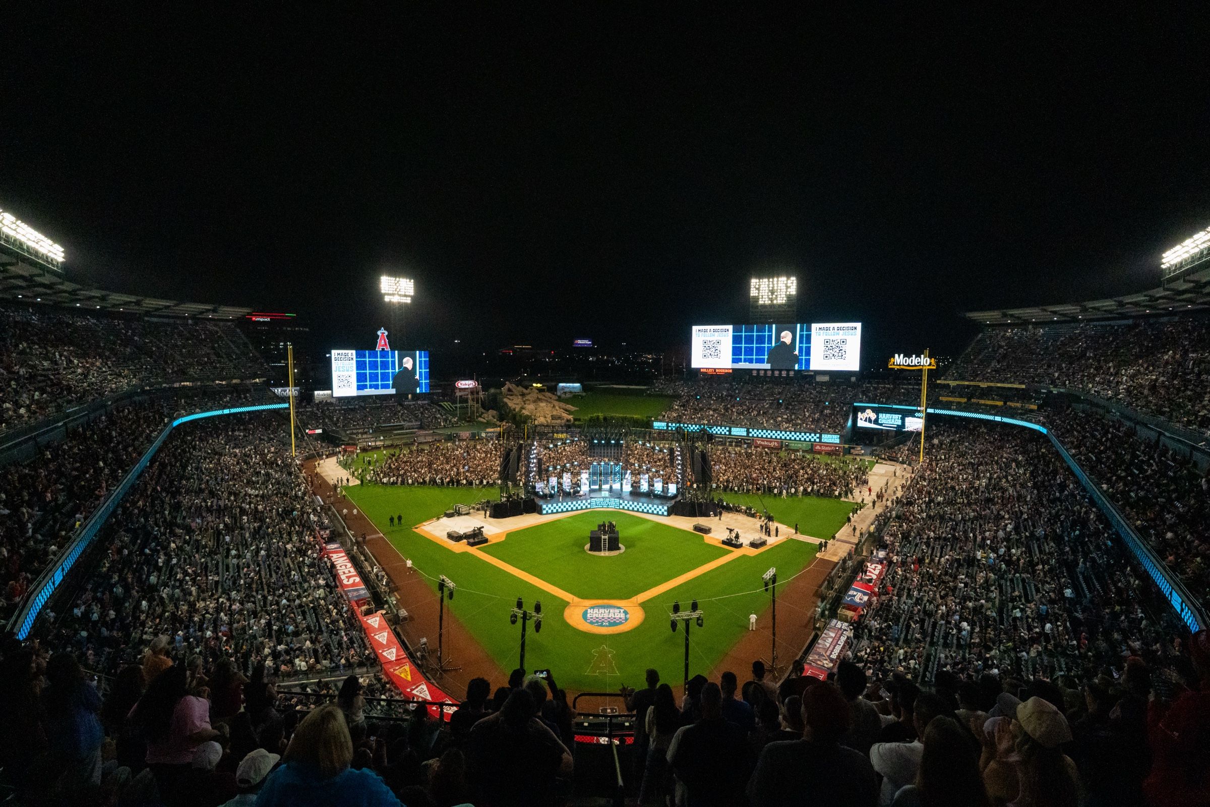 Angel Stadium at night from the upper deck during Harvest Crusade 2025 — both outfield LED screens and the ribbons lit
