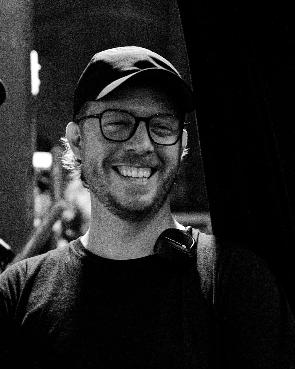 Liam Monroe backstage in a cap and glasses, laughing, radio clipped to his strap