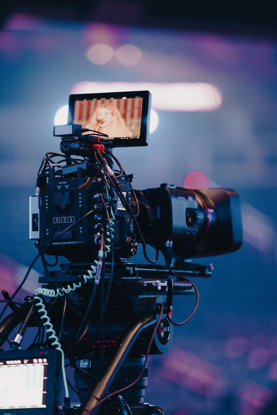 A RED Komodo on the tripod with a singer on its monitor, arena bokeh behind