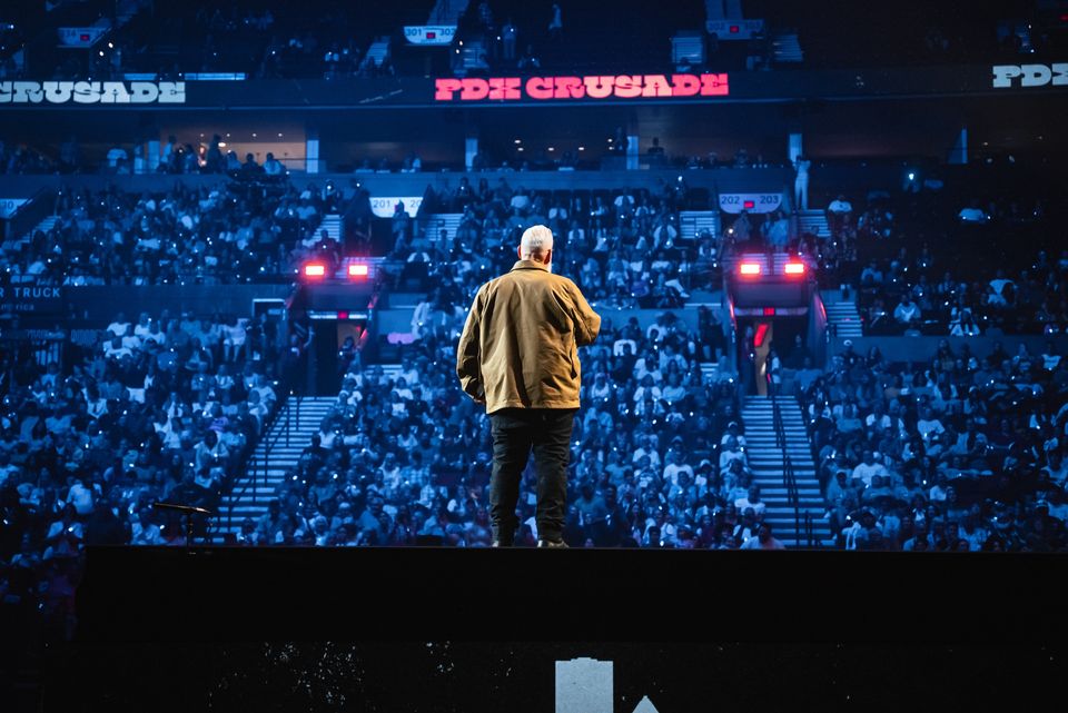 Pastor Brett Meador from behind, facing the full arena with PDX CRUSADE on the LED walls