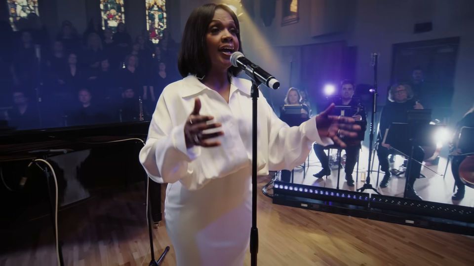 CeCe Winans singing, arms open, the strings and choir behind her
