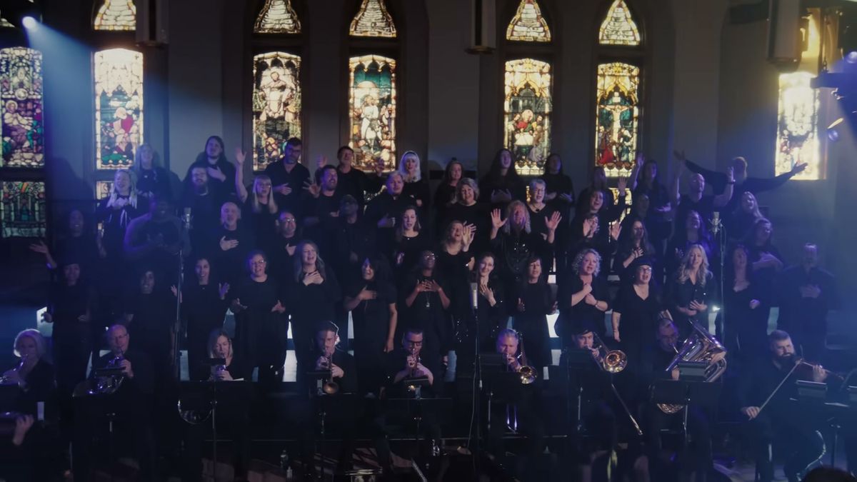 The choir under the stained glass windows of the chapel, lit blue, from the Jesus Paid It All video