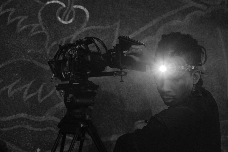A camera operator with a headlamp beside the tripod camera